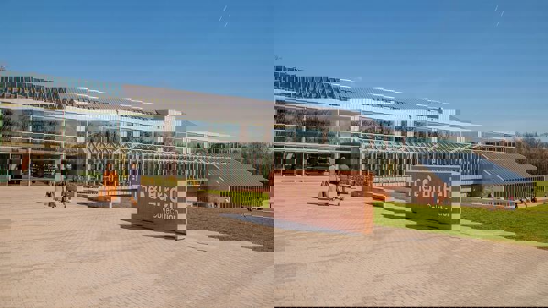 The exterior of The Burrell Collection in Glasgow. A sign reading 'The Burrell Collection' stands in front of the museum with trees behind.