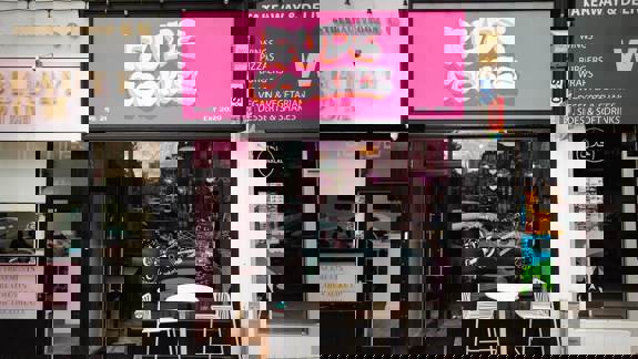 Bright pink shopfront for Rude Cookies, a dessert and coffee shop established 2020, with small white outdoor seating.