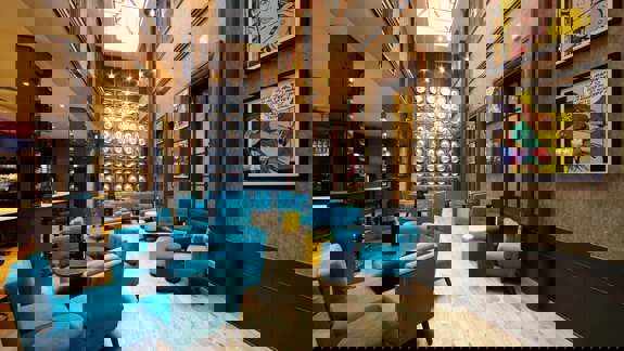 A stylish and eclectic hotel bar featuring industrial elements, vibrant red and purple furniture, exposed lighting fixtures, and a relaxed yet trendy vibe.