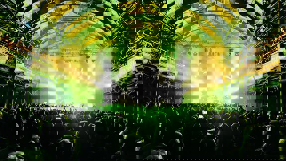 A crowded music venue with a band performing on a stage under bright spotlights, with the audience silhouetted in the foreground.