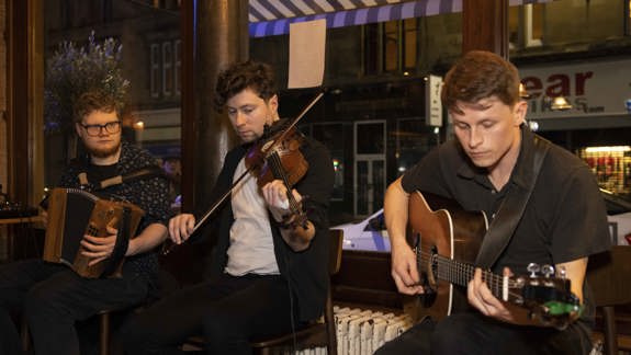 A group of three musicians playing an accordion, a fiddle, and an acoustic guitar.