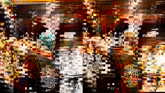 Bartender selects whisky bottles from a large, ornate shelf at The Pot Still, a traditional Glasgow whisky bar with a vast selection.