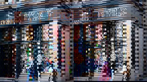 Exterior view of Mitchell's, a traditional-style sweet shop with a dark facade, large windows displaying colourful sweets, and a prominent "MITCHELL'S" sign.