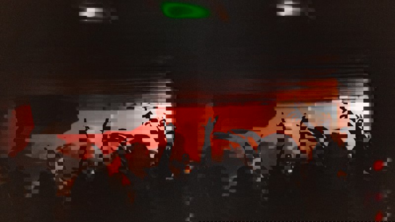 Silhouettes of club-goers with raised arms dancing in the Sub Club, lit by red stage lights and low ceilings.