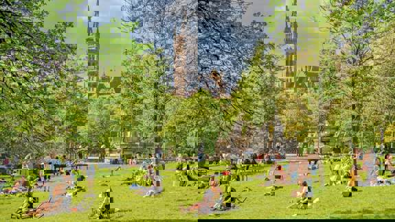 Kelvingrove Park: A park with people relaxing on the grass on a sunny day, with the University of Glasgow building visible in the background.