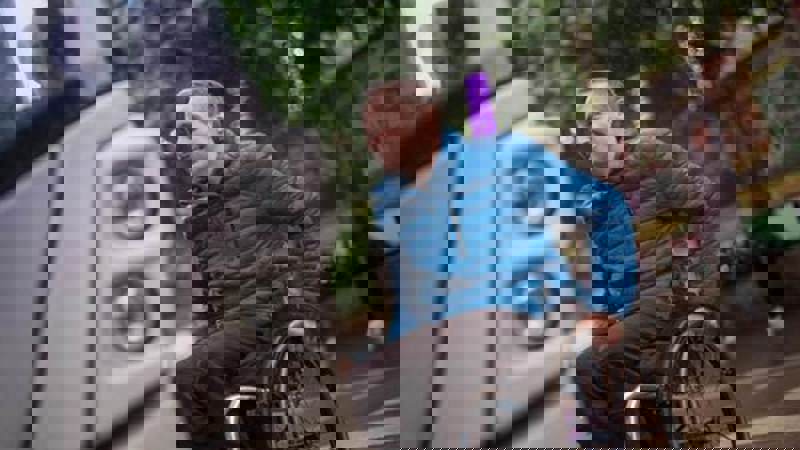 A person in a wheelchair smiles as they are about to board a bus, which is partially visible on the left.