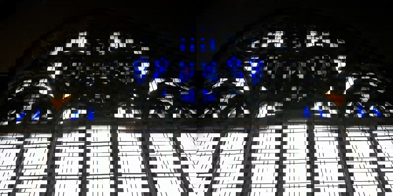 Stained-glass window with geometric and floral patterns, featuring prominent blue and clear glass sections.