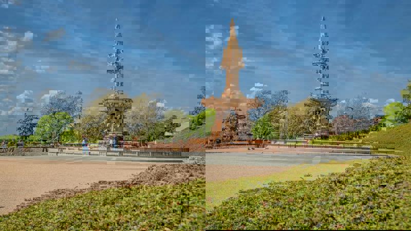 A ornate terracotta fountain, the Doulton Fountain, sits in a plaza with trees and people in the background under a blue sky.