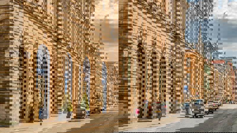 A sunlit street scene in Glasgow with a large, ornate building housing a Ralph Lauren store and traffic moving along the road.