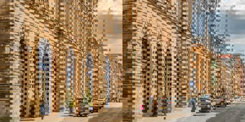 A sunlit street scene in Glasgow with a large, ornate building housing a Ralph Lauren store and traffic moving along the road.