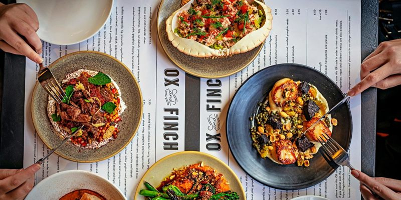 An overhead view of four people dining, with multiple plates of food on the table, including crab and scallops.