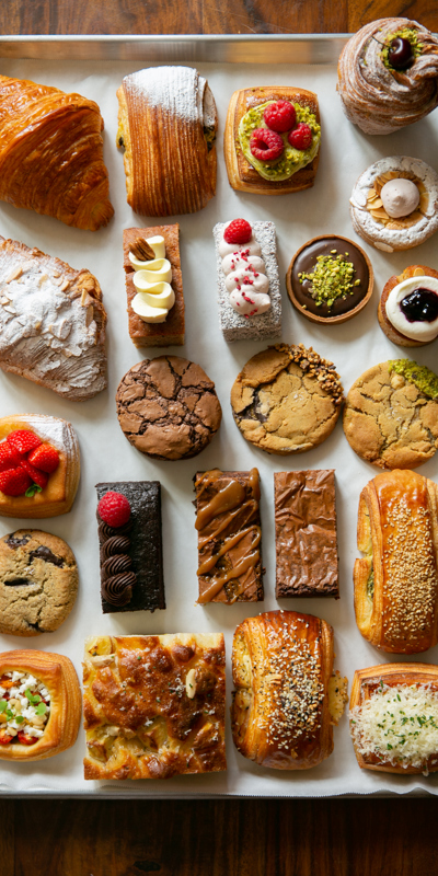 An overhead view of an assortment of pastries and desserts neatly arranged on a baking tray, including croissants, cookies, tarts, and cakes.