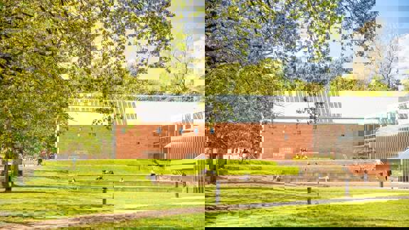A daytime shot of The Burrell Collection museum. The red-brick and glass-roof building sits on a green lawn in a park setting.