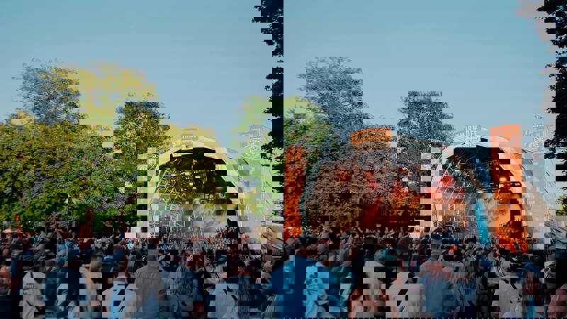 A wide-angle shot of a music festival stage during the daytime, with a crowd of people watching the performance.