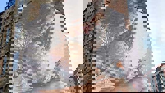 Large mural on a building showing a woman holding a baby, with a small robin perched nearby.