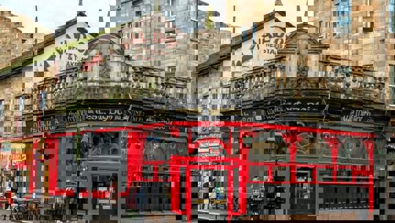 Exterior view of a traditional, historic pub called "The Tolbooth Bar est. 1906" on a street corner, with a striking black and red facade.