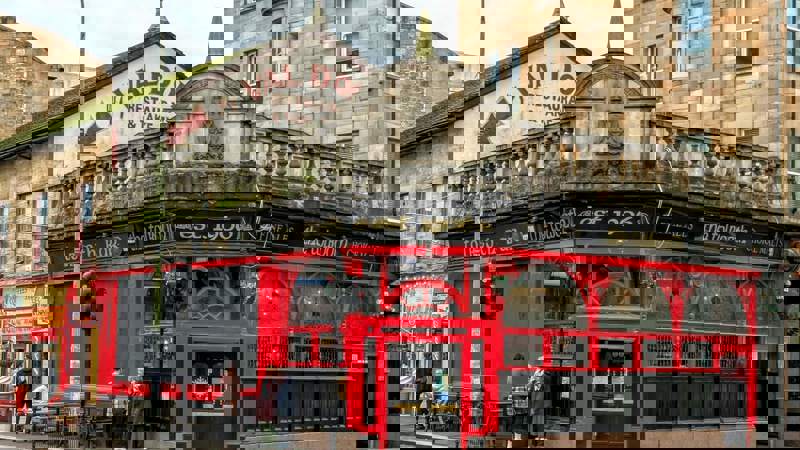 Exterior view of a traditional, historic pub called "The Tolbooth Bar est. 1906" on a street corner, with a striking black and red facade.