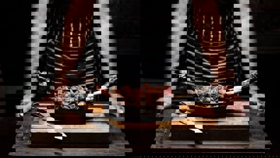 Person behind a cutting board with sliced steak on the bone and a knife.