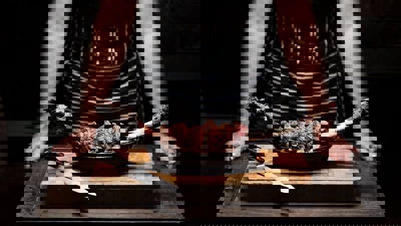 Person behind a cutting board with sliced steak on the bone and a knife.