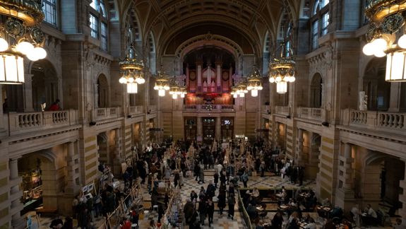 Busy craft market inside Kelvingrove Art Gallery and Museum, with stalls lining the grand hall and visitors walking through the space beneath ornate lighting