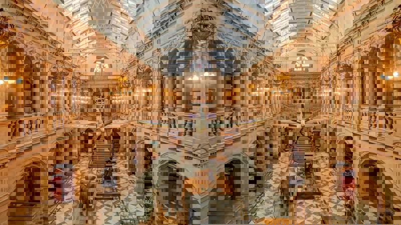 The grand, vaulted interior of a museum with a plane suspended from the ceiling and taxidermy animals, including an elephant and a giraffe, on the floor.