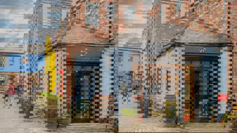 A cobbled alleyway with colourful buildings, including a small blue shop with a sign that reads "25."