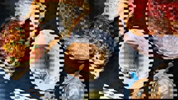 An overhead shot of a table with a skillet of shakshuka, a roll, French toast with strawberries, and two coffee drinks.