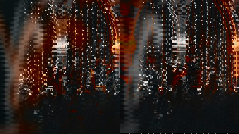 Audience watching a candlelit string quartet performance inside Òran Mór, with fairy lights and arched stone architecture.