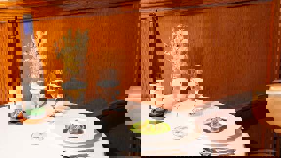 A small round table with a single plate of food, a bottle of wine, and two glasses.