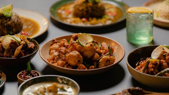 A table set with several Sri Lankan dishes in bowls, including spiced fried vegetables and curries, garnished with lime slices.