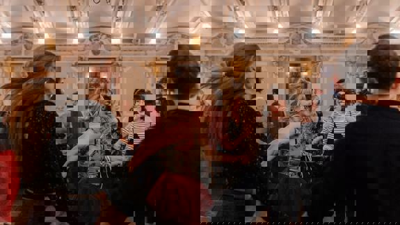 A joyful Scottish ceilidh dance in a grand, ornate hall. People hold hands, spinning and laughing in a lively atmosphere under chandeliers.