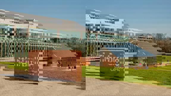 A modern museum building with large glass windows and a prominent stone sign that reads "The Burrell Collection" in front of a grassy lawn.