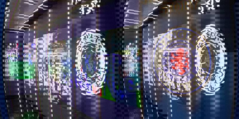 An interior shot of a football museum with a large illuminated Rangers FC crest and "The Rangers Story" sign on the wall.