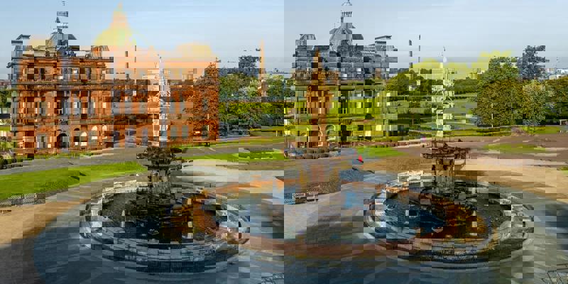 An aerial view of the Doulton Fountain in Glasgow Green with a grand building and park in the background.
