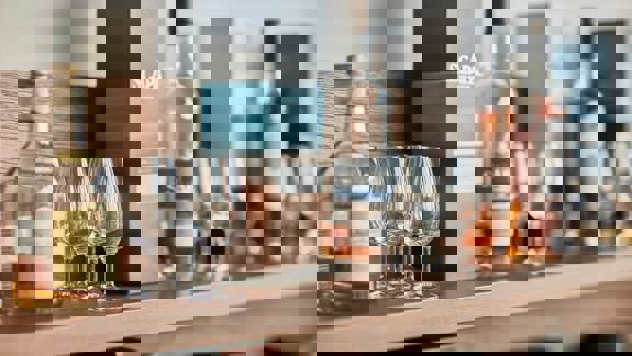 Inside the Clydeside Distillery, large, gleaming copper stills are shown with a view of the River Clyde and a tall ship through the floor-to-ceiling windows.