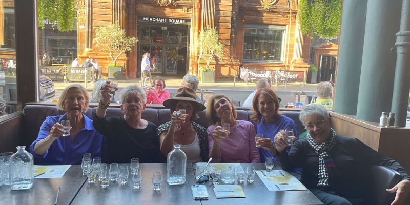 A group of people toasting with whisky glasses at a table in a pub.