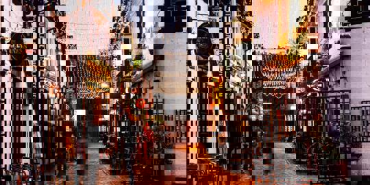 A charming cobbled alleyway in Glasgow's West End, lined with twinkling fairy lights and pubs, captured at dusk. 