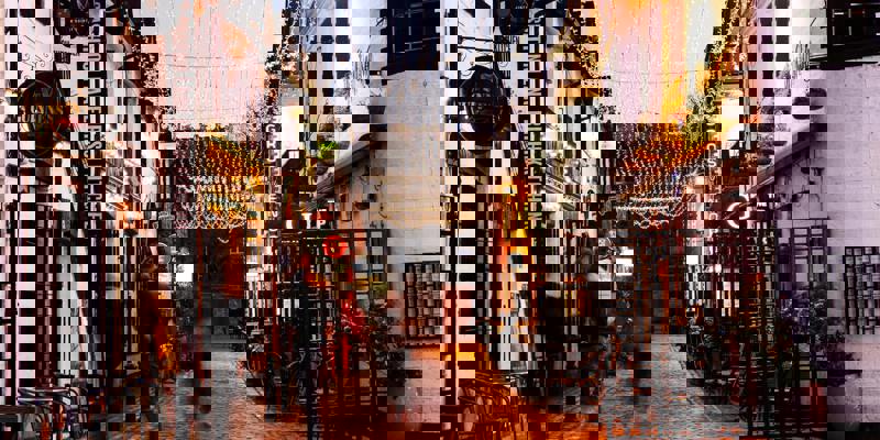 A charming cobbled alleyway in Glasgow's West End, lined with twinkling fairy lights and pubs, captured at dusk.