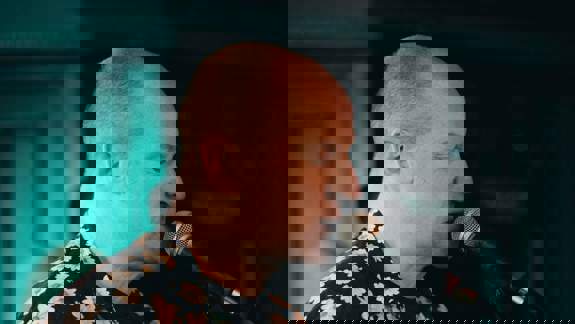 A man with a shaved head plays an electric guitar and sings into a microphone while performing.