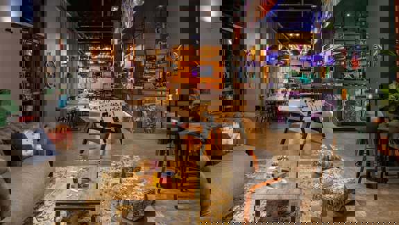 A playful, youthful bar with bright neon signage, exposed ceilings, mismatched seating, and an open-plan space that feels casual and social.