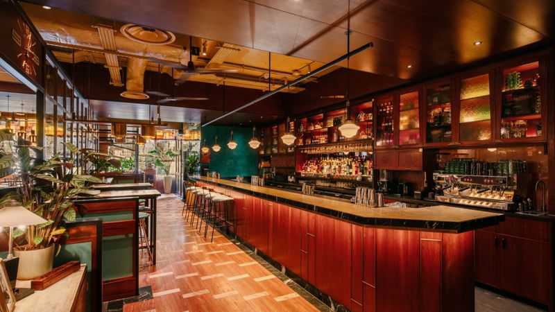Warm and stylish bar interior with wooden furnishings, hanging lights, and a long counter at Dishoom restaurant in Glasgow