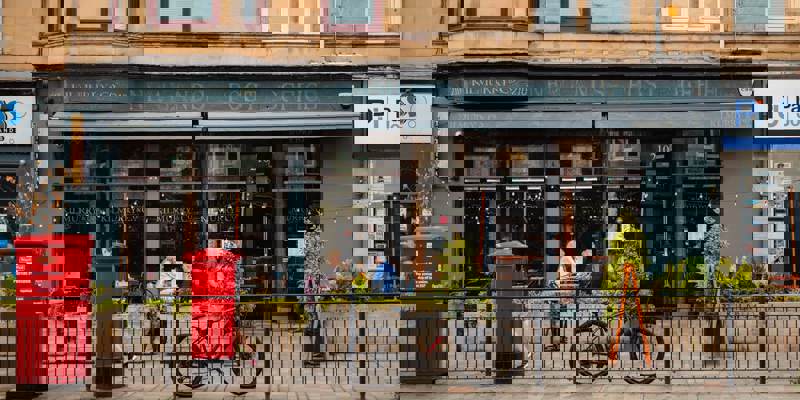 Exterior of Kilmurry & Co, a cafe with old exposed signage reading 'Newlands Post Office'. A bicycle and red post box sit in front of the cafe's outdoor seating area.