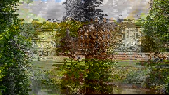 A grand manor house overlooking a river and lush green trees in Pollok Park, Glasgow.