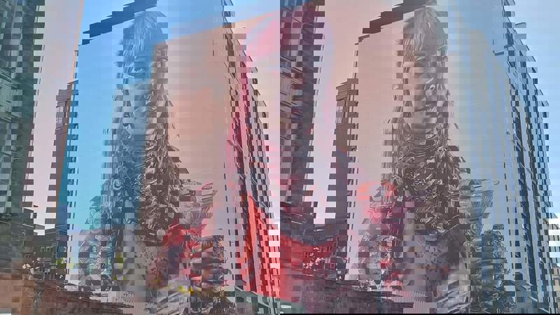 A large, colourful mural on the side of a building, depicting a person with pink hair holding a cocktail and a candle.