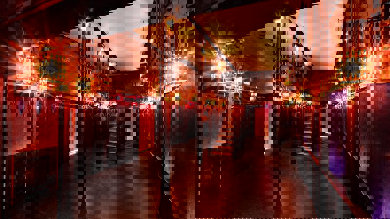 A dimly lit, wood-paneled room with intricate geometric light fixtures and a staircase, showcasing the distinct style of Charles Rennie Mackintosh's Oak Room.