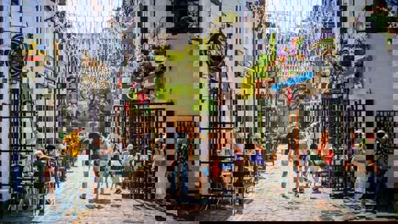 A cobblestone street lined with pubs and restaurants, with people dining outdoors under hanging lights.