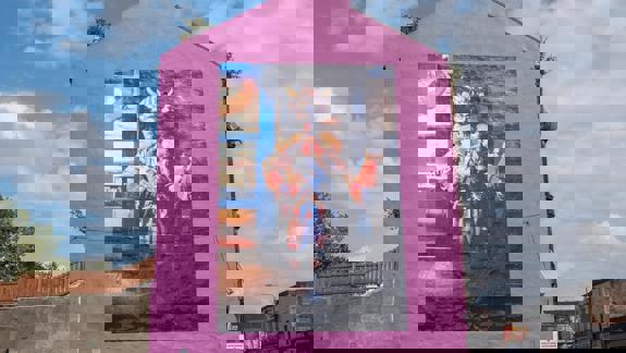 Bright pink building with a large mural of Billy Connolly in a fantastical, colourful costume with a horned helmet.