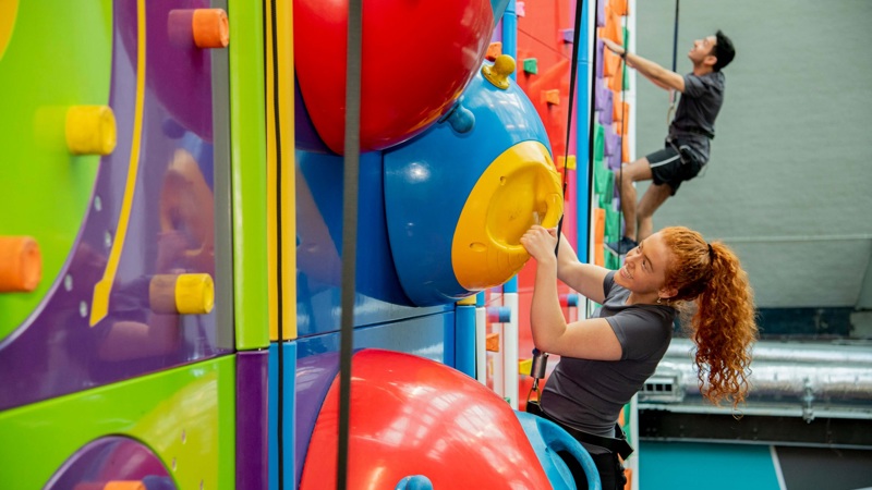 Two people scale a colourful indoor climbing wall.