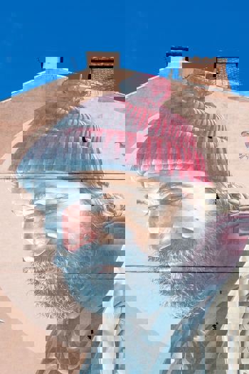 Mural on a gable end showing a man known as St Mungo with a beard and red bobble hat looking down at a robin.