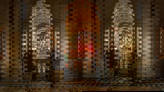 People stand on a balcony with a checkered floor, looking at a large, ornate organ in a grand hall.